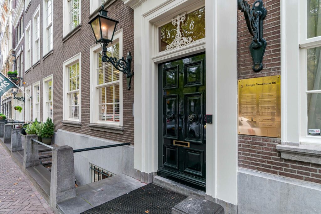 Ingang van een statig pand aan Lange Voorhout 86 met donkere voordeur, gevelverlichting en bedrijfsnaamplaat.